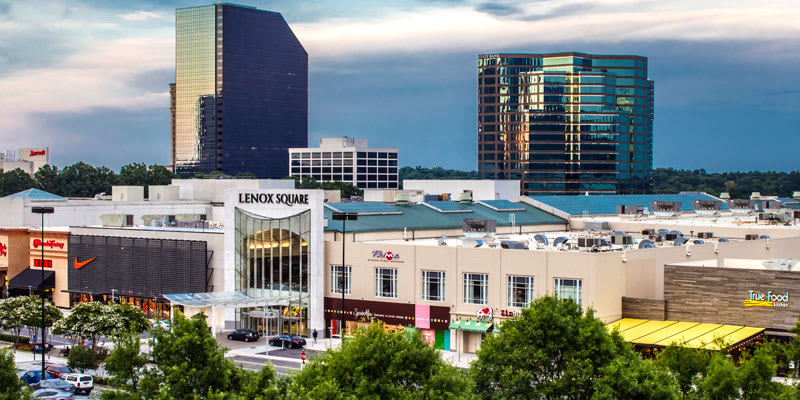 A bustling cityscape at dusk with modern skyscrapers, a shopping mall, and lush green trees in Atlanta, Georgia.