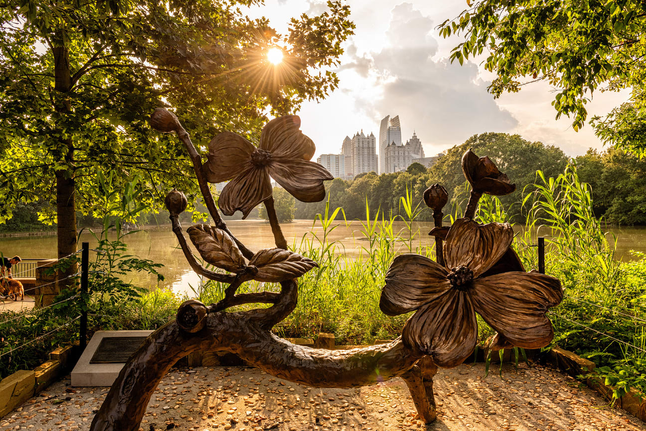 A large bronze sculpture of a tree branch with giant flowers overlooks a serene lake at sunset in Atlanta, Georgia.