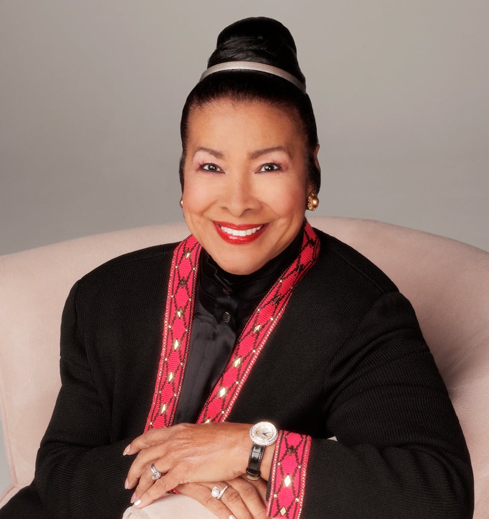 A woman with an elegant updo and a radiant smile wears a black outfit with a red and gold patterned collar in Atlanta, Georgia.