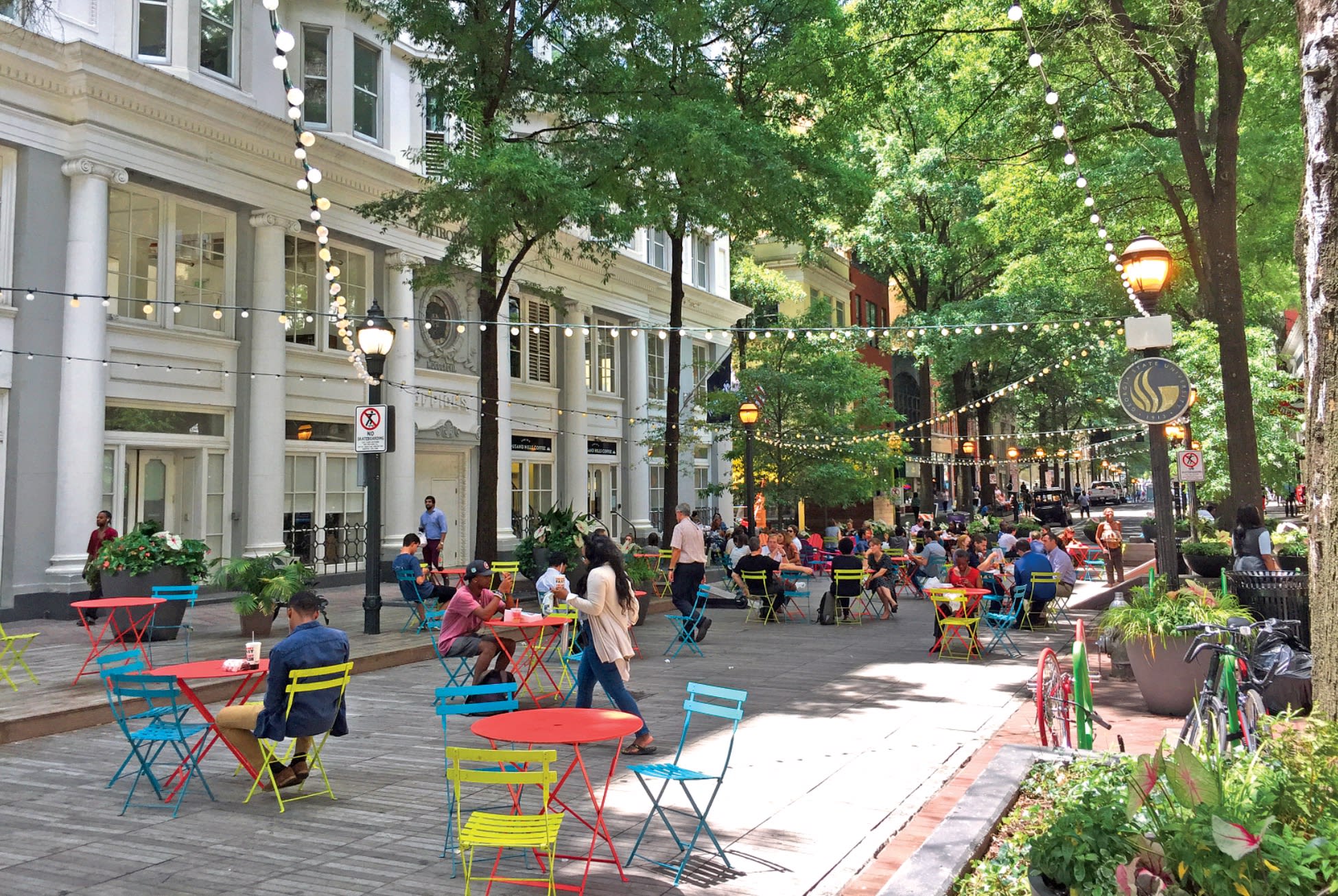 A vibrant outdoor cafe scene with colorful tables and chairs, surrounded by lush greenery and historic buildings in Atlanta, Georgia.