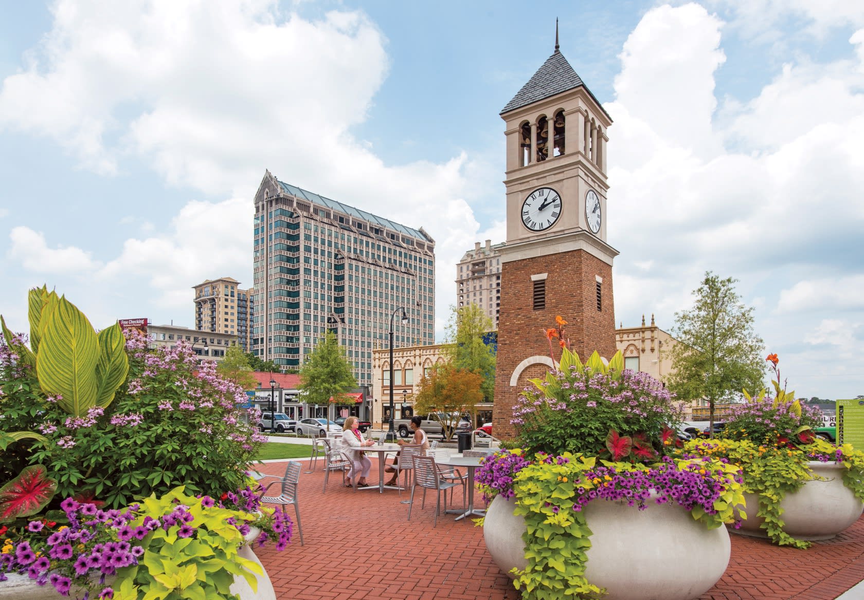 A vibrant city square with a clock tower, surrounded by colorful flower beds and people enjoying outdoor cafes in Atlanta, Georgia.