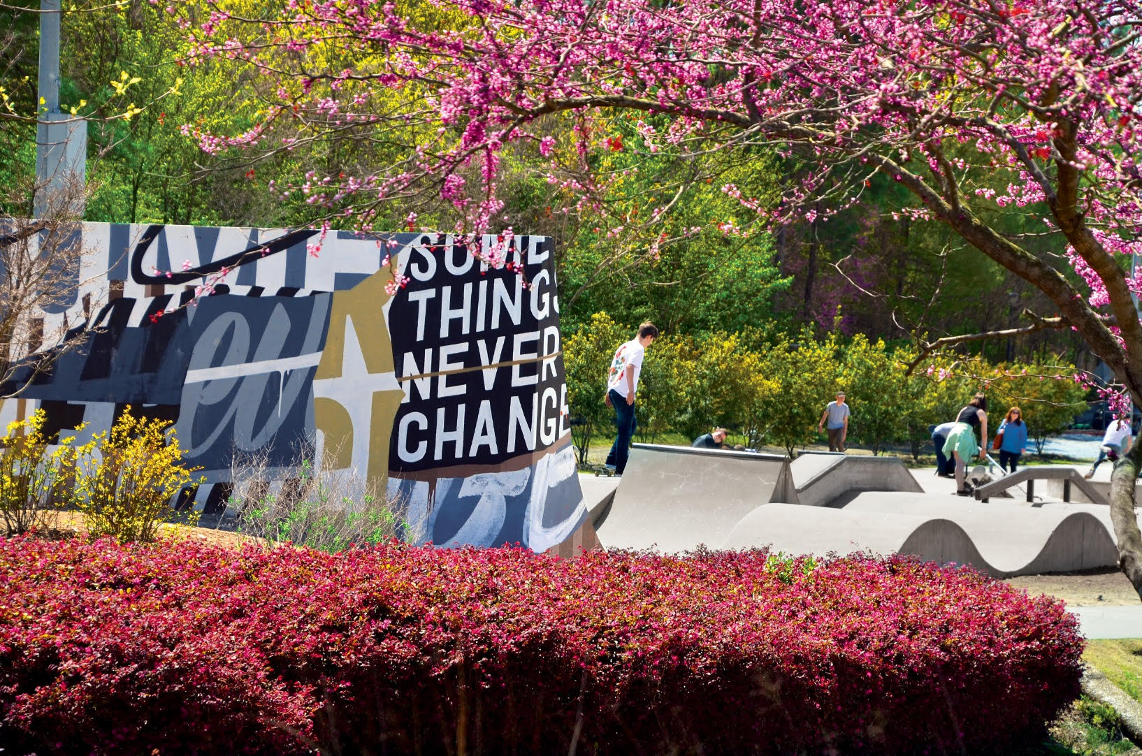 A colorful mural with motivational text adorns a skate park surrounded by lush greenery and blooming trees in Atlanta, Georgia.