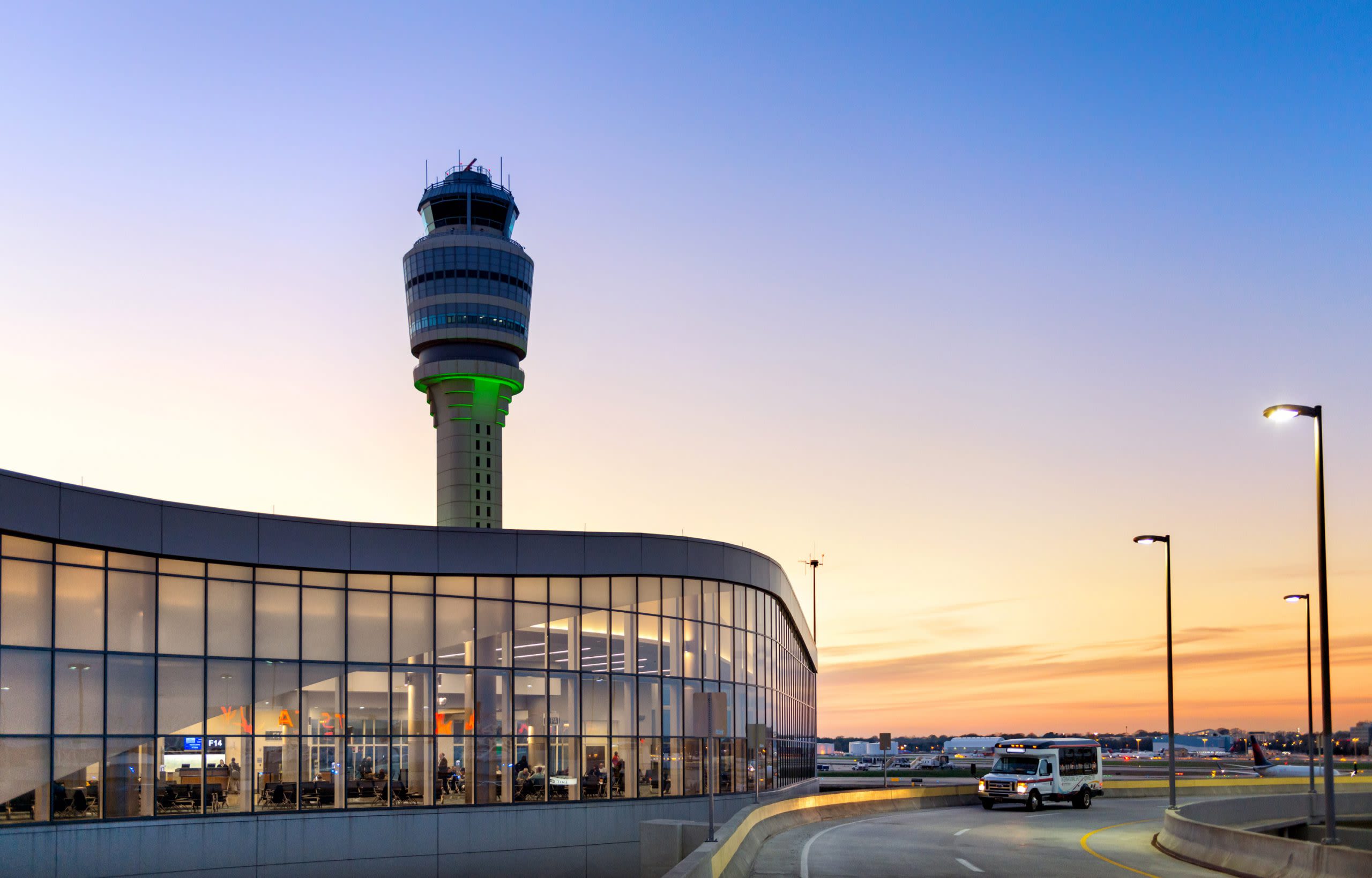 Modern airport terminal with curved glass facade and illuminated control tower at dusk in Atlanta, Georgia.