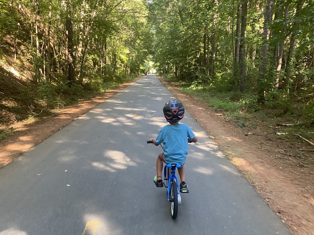 A child in a blue shirt and helmet rides a bike down a tree-lined path in Atlanta, Georgia.