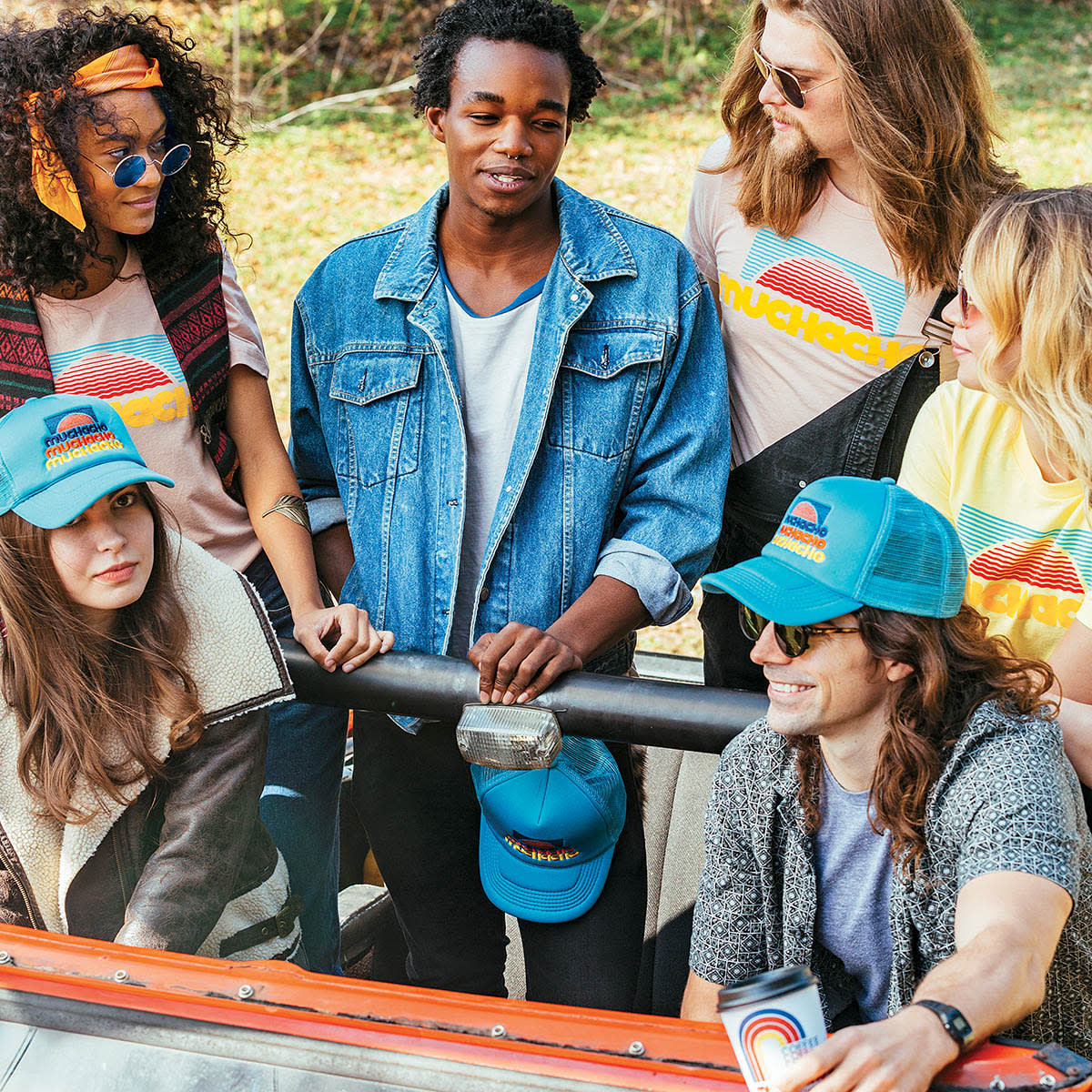 A group of six young adults, dressed in casual, colorful clothing, are smiling and posing together in a convertible car in Atlanta, Georgia.