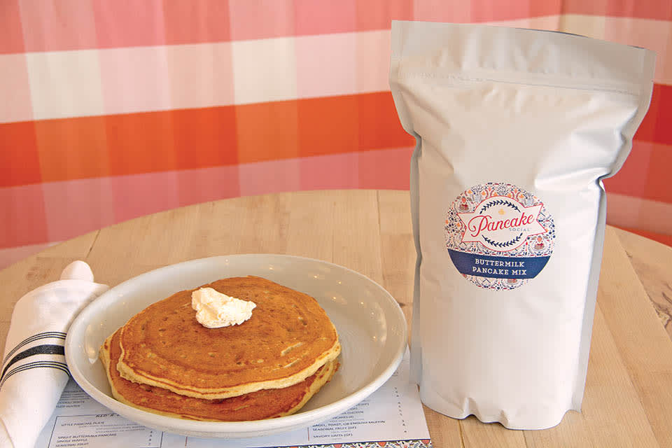 Stack of pancakes with butter and syrup on a plate next to a bag of pancake mix in Atlanta, Georgia.