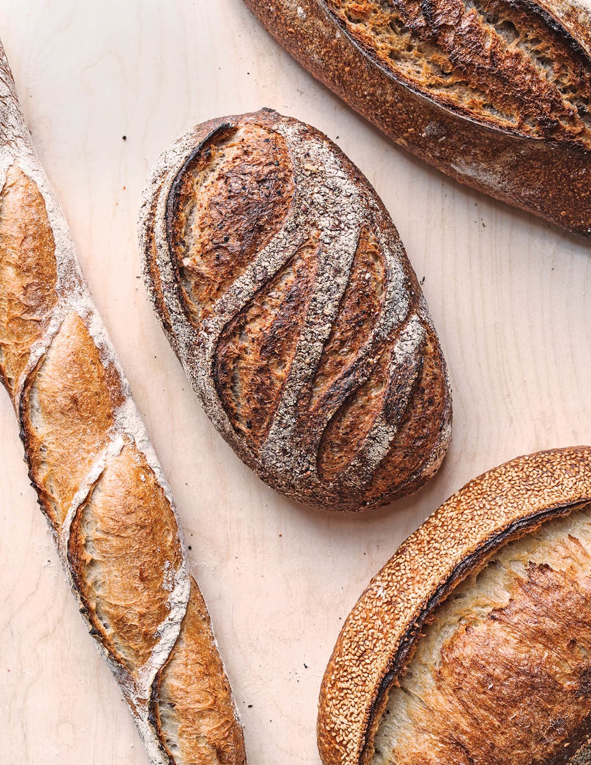 Four artisanal breads, including baguettes and round loaves, are arranged on a wooden surface in Atlanta, Georgia.