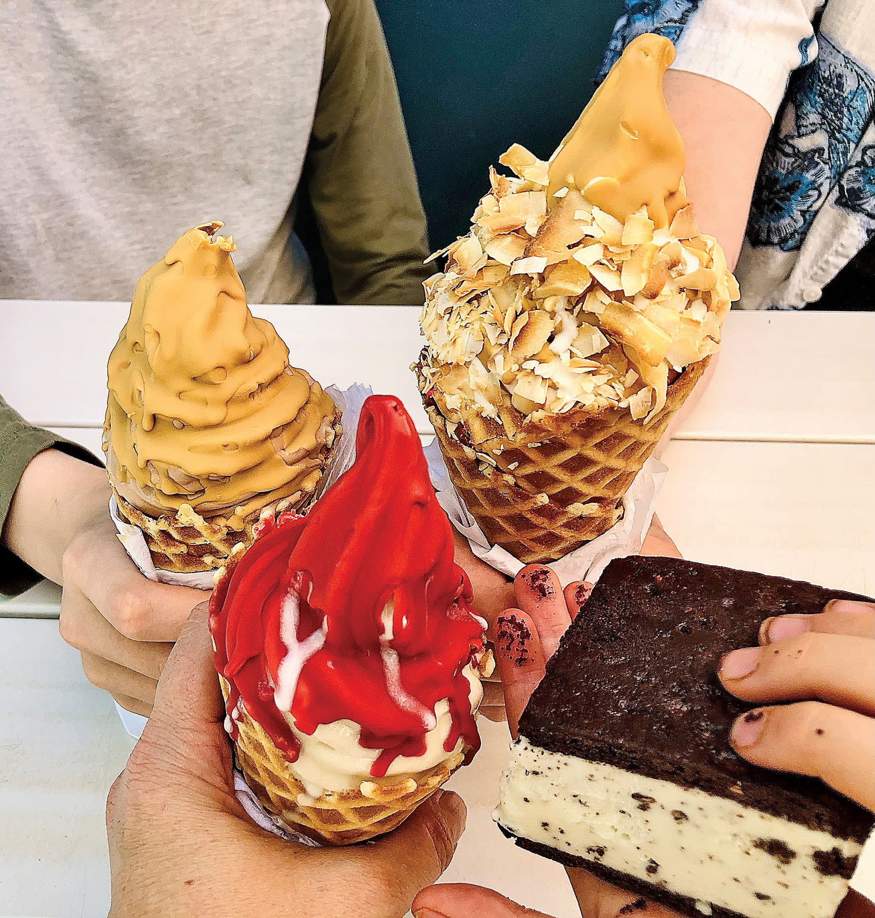 Four hands hold ice cream cones with various toppings and a chocolate bar in Atlanta, Georgia.