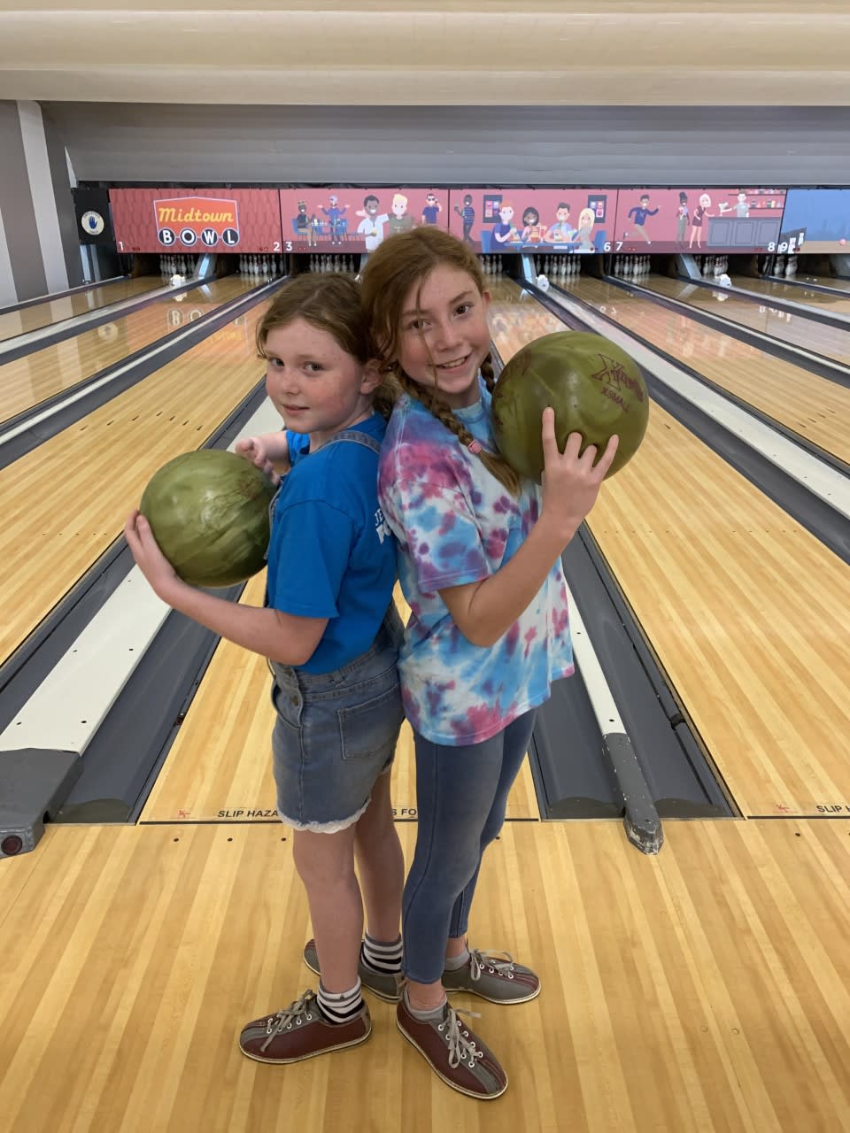 Two young girls, dressed in casual attire, proudly hold bowling balls at a bowling alley in Atlanta, Georgia.