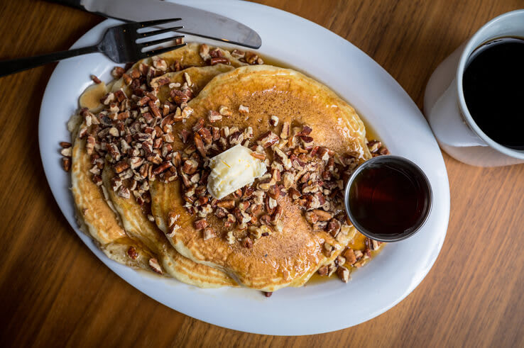 Stack of pancakes topped with butter, chopped nuts, and syrup, served with coffee in Atlanta, Georgia.