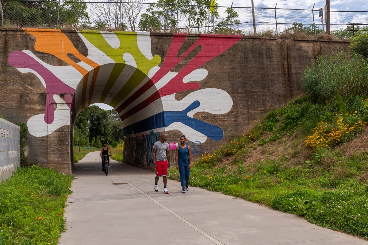 People walk and bike through a colorful tunnel under a bridge surrounded by nature in Atlanta, Georgia.