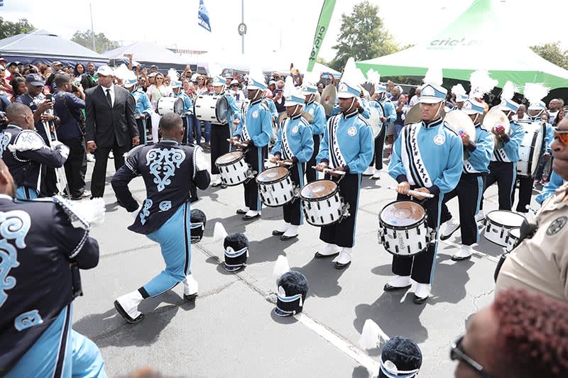 A marching band in blue and white uniforms performs for a large crowd at an outdoor event in Atlanta, Georgia.