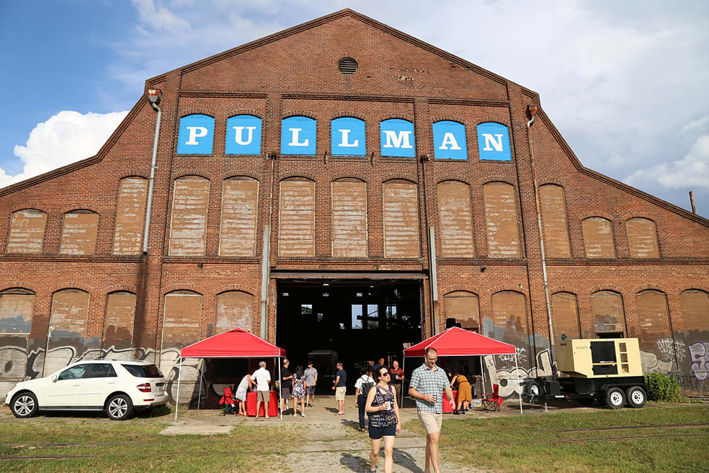 A large brick warehouse with 'PULLMAN' painted on it hosts an outdoor event with red tents and people in Atlanta, Georgia.