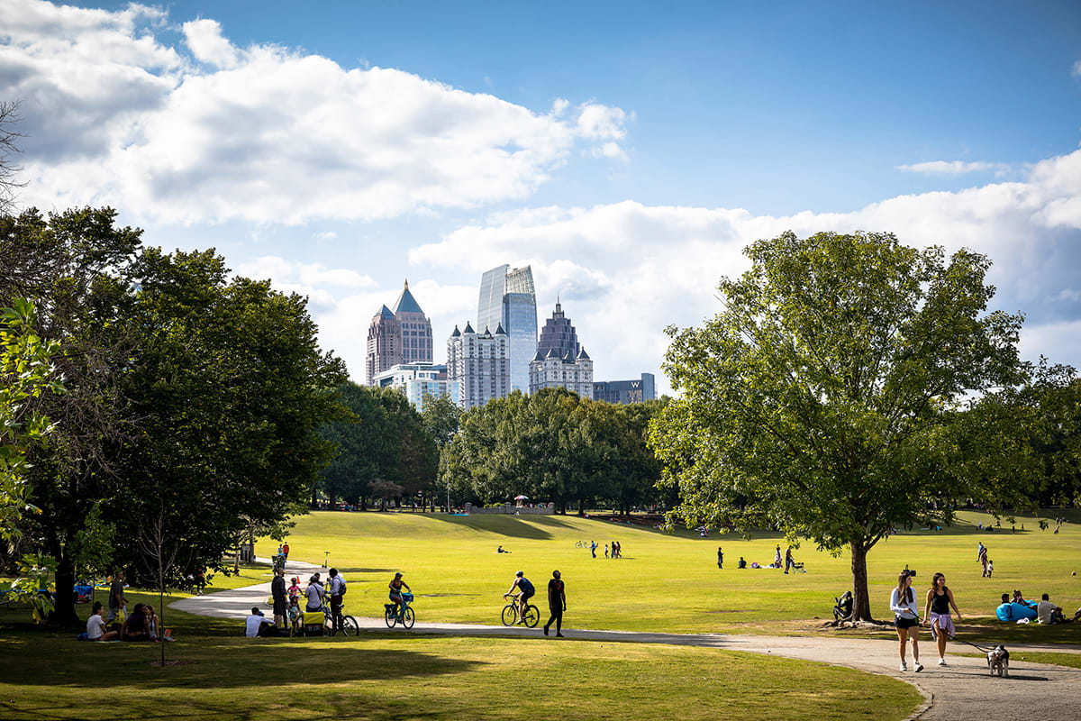 A bustling city park with cyclists, pedestrians, and picnickers under a clear blue sky in Atlanta, Georgia.