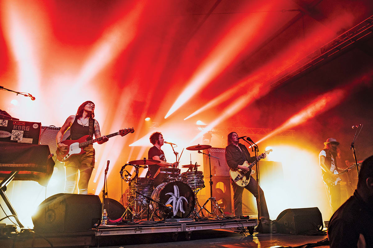 A band performs on stage with vibrant red lighting, featuring guitars, drums, and a keyboard in Atlanta, Georgia.