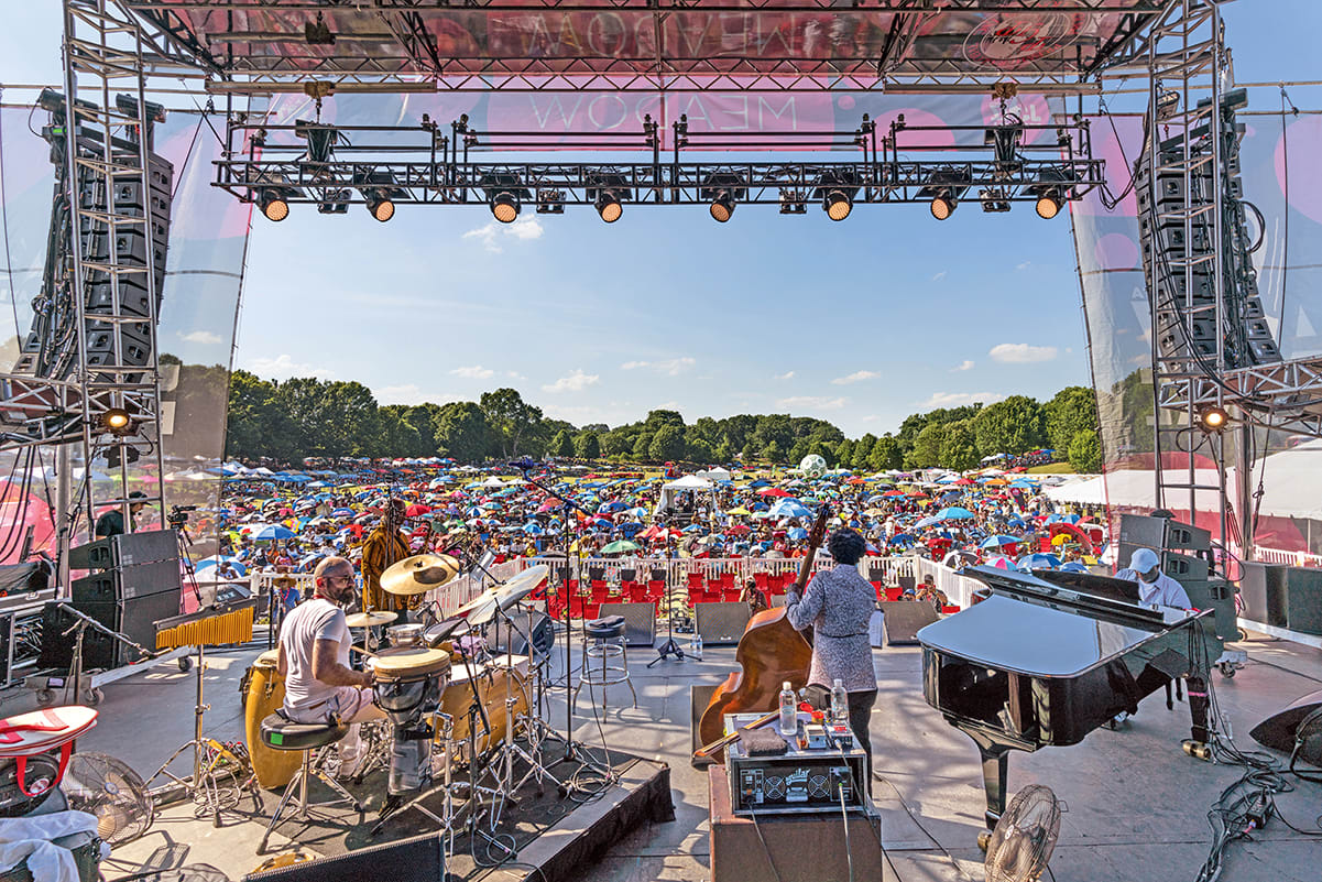 A crowded outdoor music festival with a large stage, musicians, and a sea of colorful umbrellas in Atlanta, Georgia.