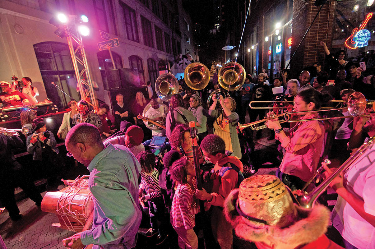 A vibrant nighttime street festival with a brass band, colorful costumes, and a lively crowd in Atlanta, Georgia.