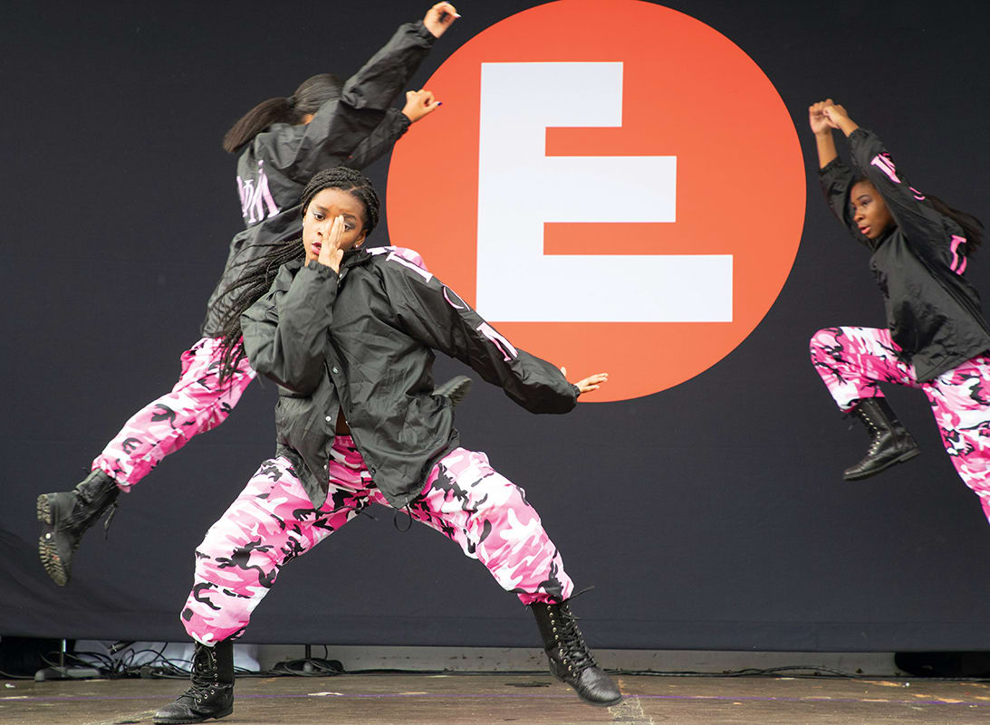 Three dancers in black jackets and pink camouflage pants perform dynamic poses on stage in Atlanta, Georgia.