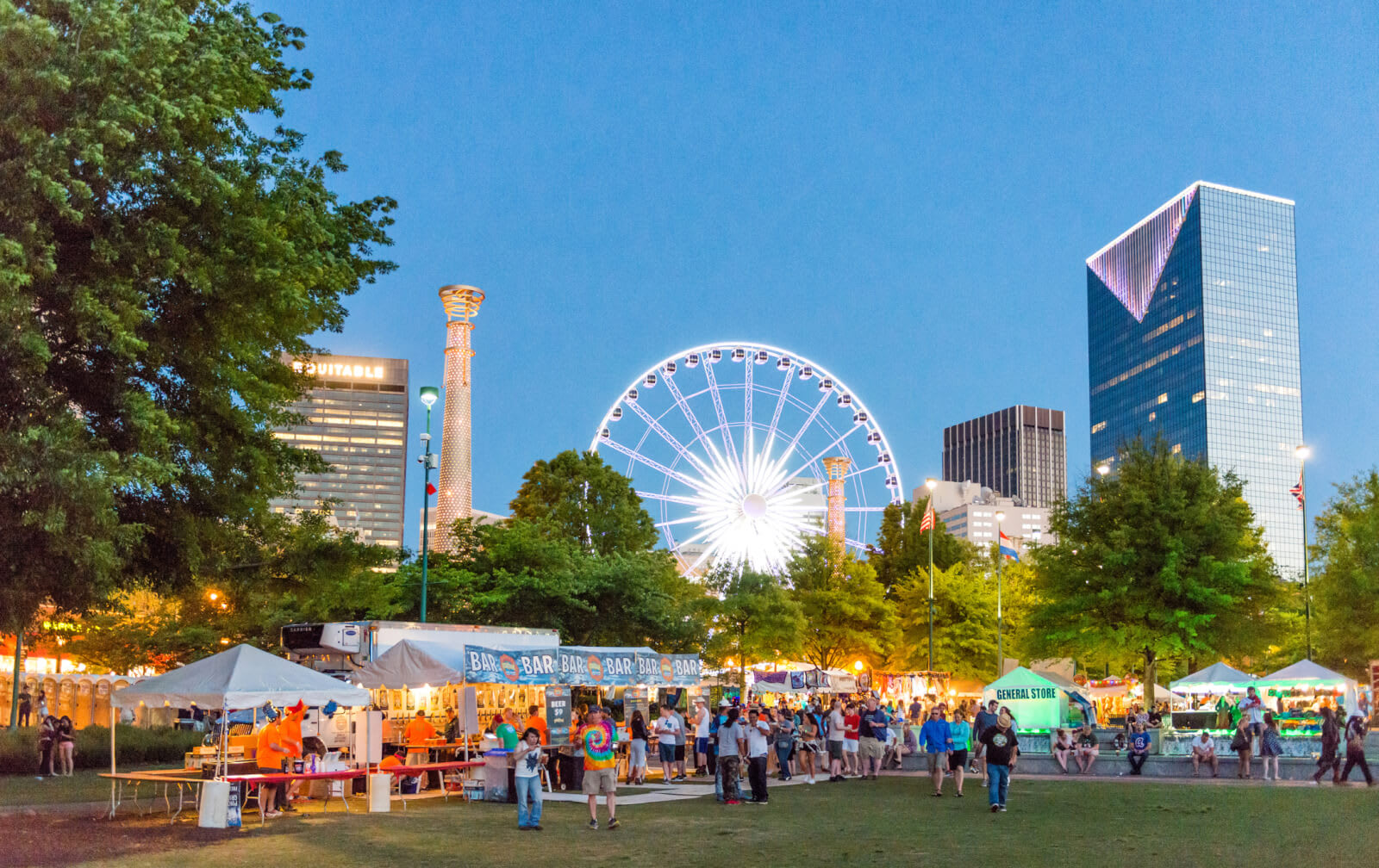 A vibrant evening festival with a Ferris wheel, food trucks, and crowds in a city park in Atlanta, Georgia.