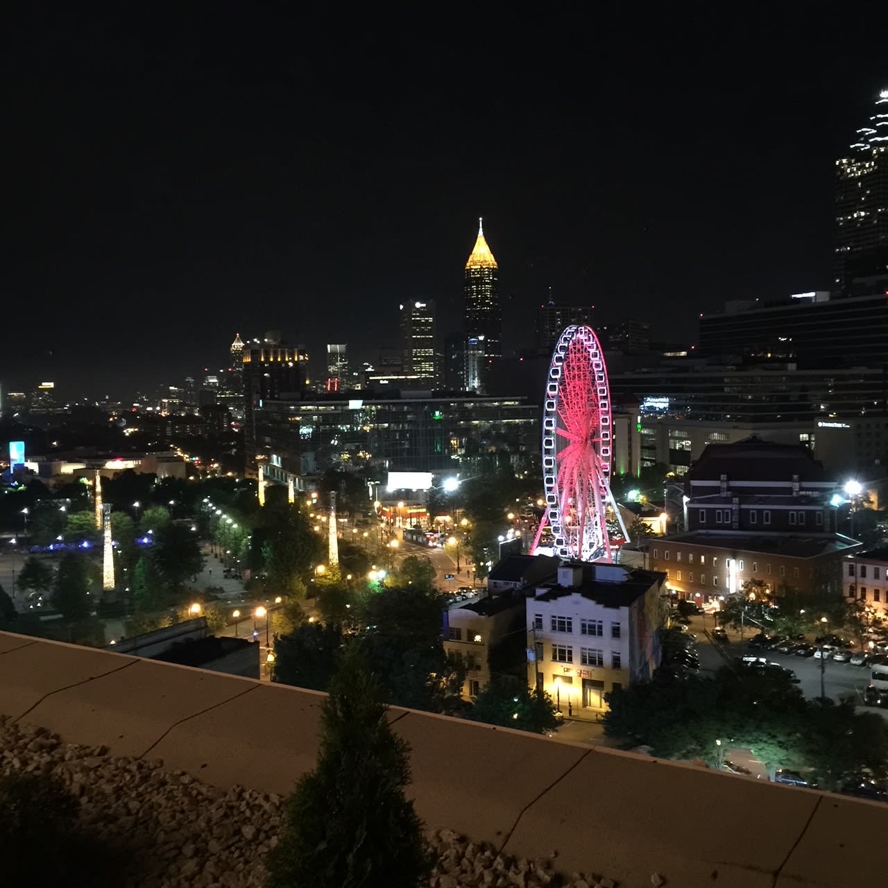 A nighttime cityscape featuring a large illuminated Ferris wheel and a distinctive skyscraper in Atlanta, Georgia.