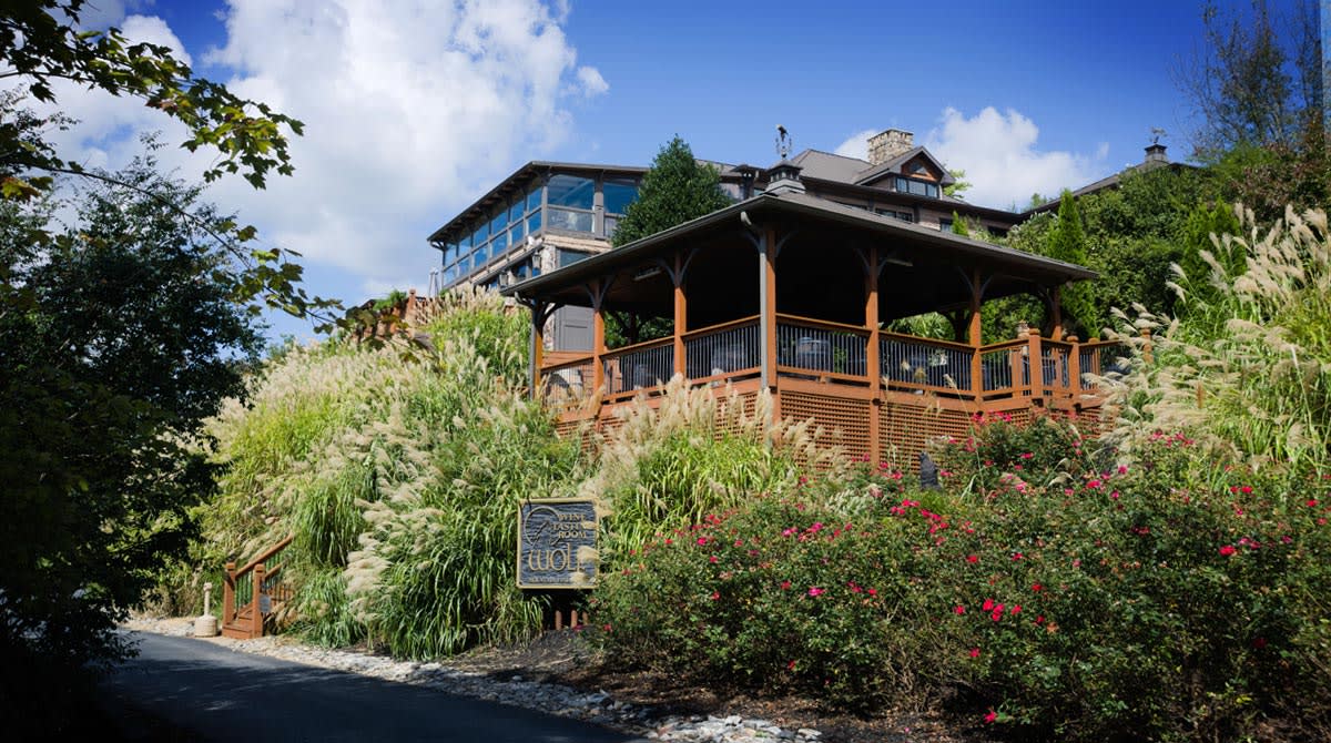 A multi-story wooden house with a wrap-around porch is nestled among lush greenery and flowers in Atlanta, Georgia.