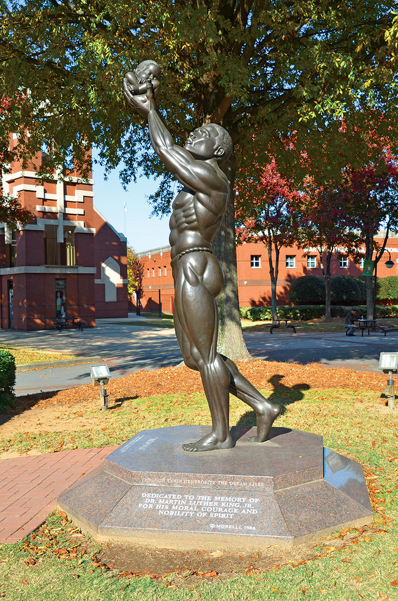 A muscular bronze statue of a man holding a baby, standing on a pedestal with an inscription in Atlanta, Georgia.