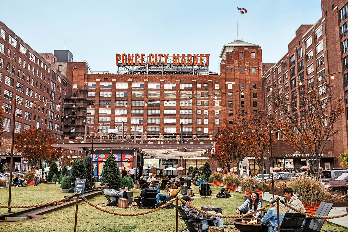 Outdoor market with people sitting around fire pits, surrounded by brick buildings and string lights in Atlanta, Georgia.