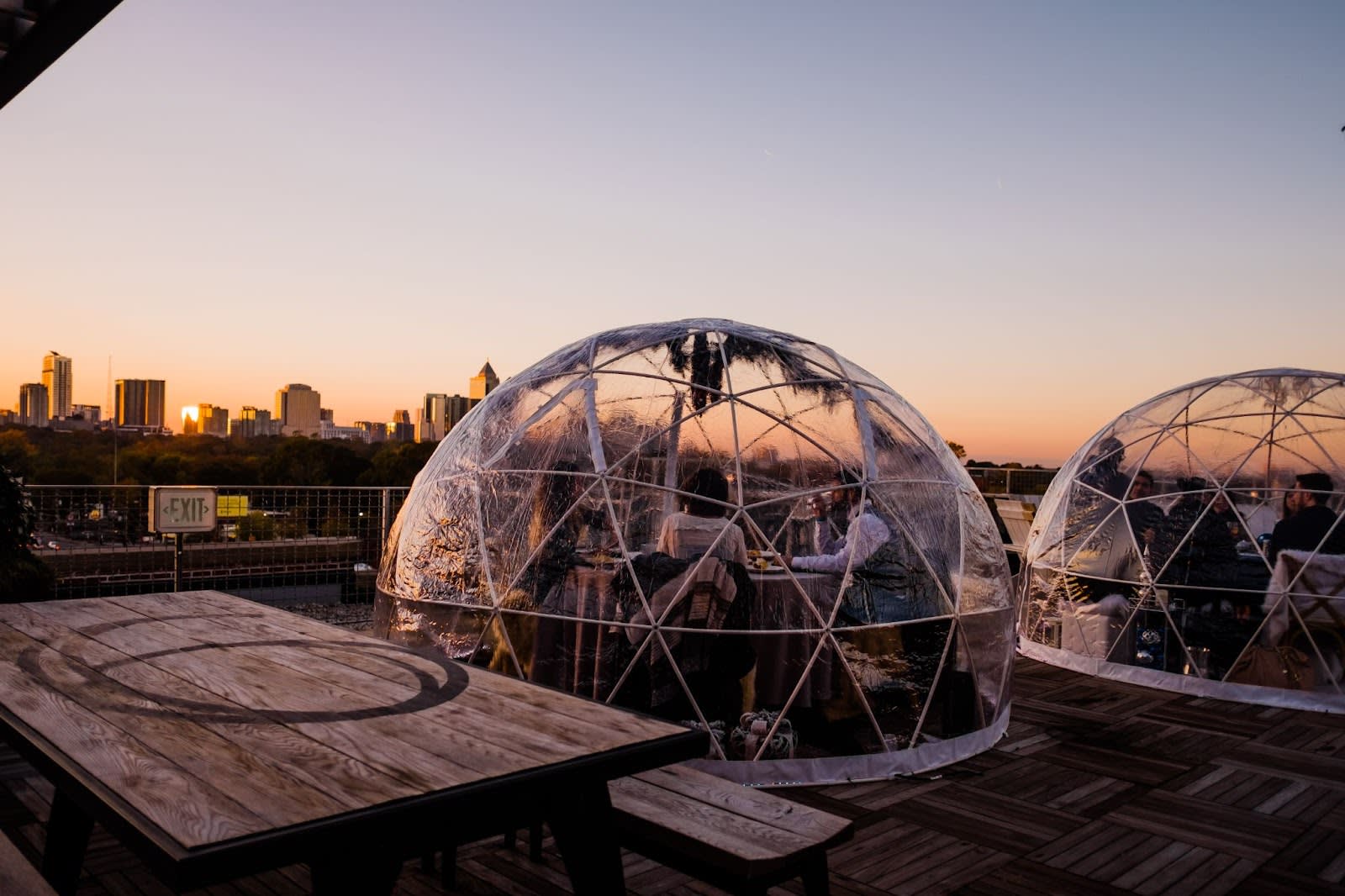 People dining in transparent geodesic domes on a rooftop at sunset in Atlanta, Georgia.