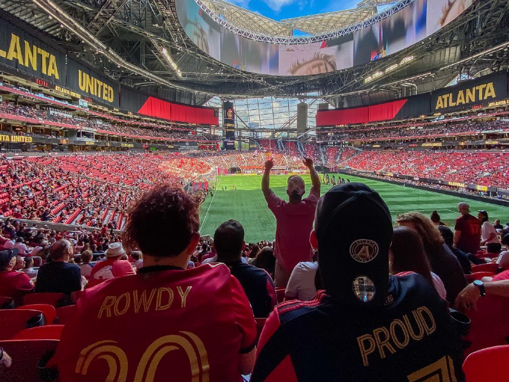 A crowded stadium with fans wearing red jerseys, cheering and raising their arms in Atlanta, Georgia.