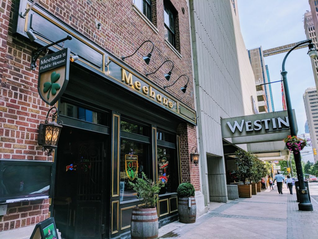 A brick building with a green shamrock sign and hanging flower baskets next to a modern hotel in Atlanta, Georgia.