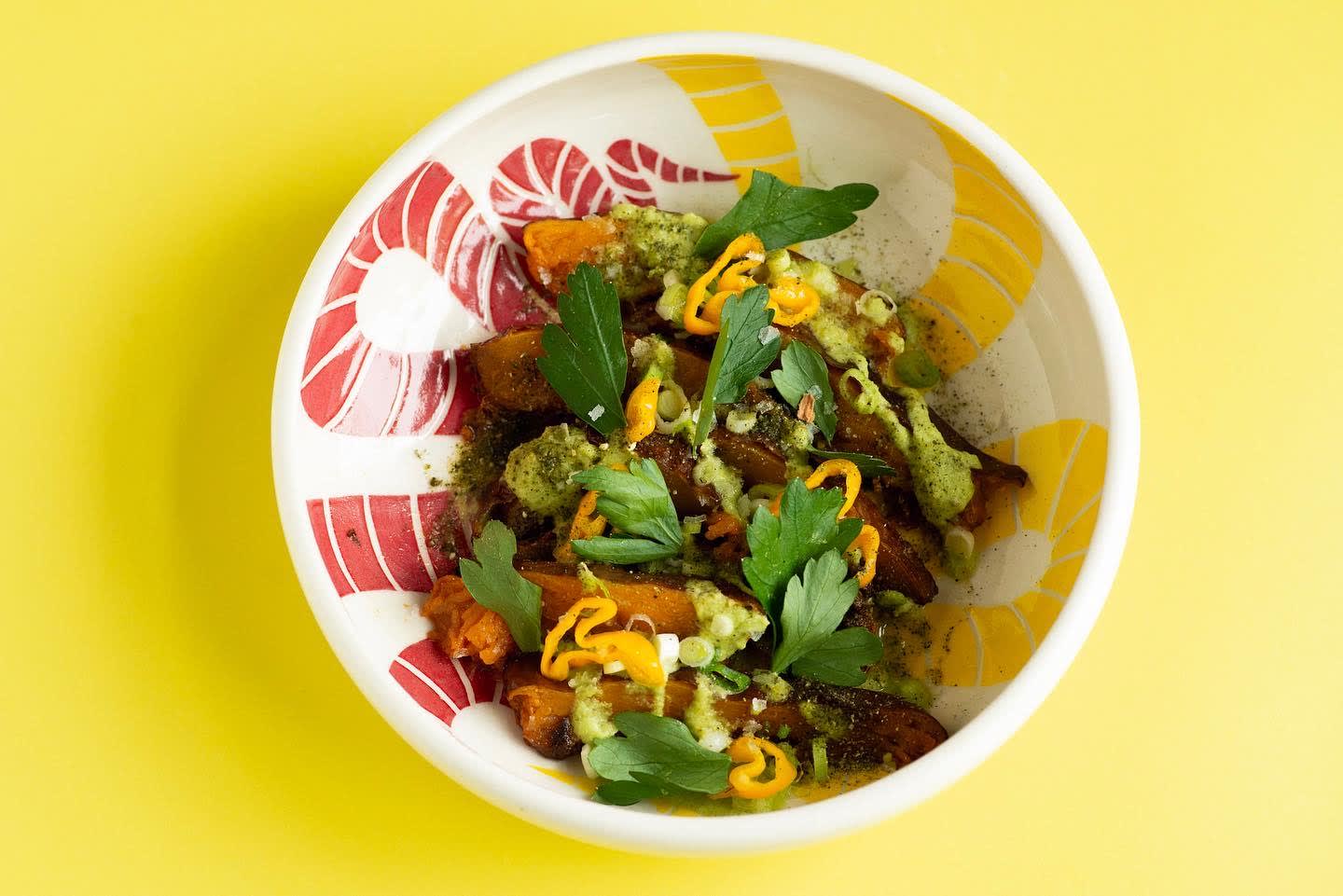 A colorful bowl filled with roasted vegetables, topped with a green sauce and fresh herbs in Atlanta, Georgia.