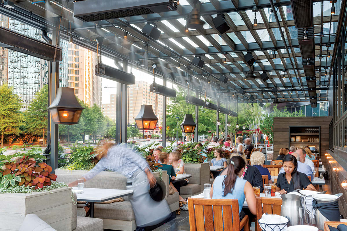 A bustling rooftop restaurant with patrons dining al fresco under a glass canopy in Atlanta, Georgia.