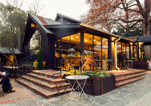 Warm up at the Best Restaurants for Cozy Winter Dining in Atlanta 3 A rustic black building with large windows and a stone patio surrounded by trees in Atlanta, Georgia.