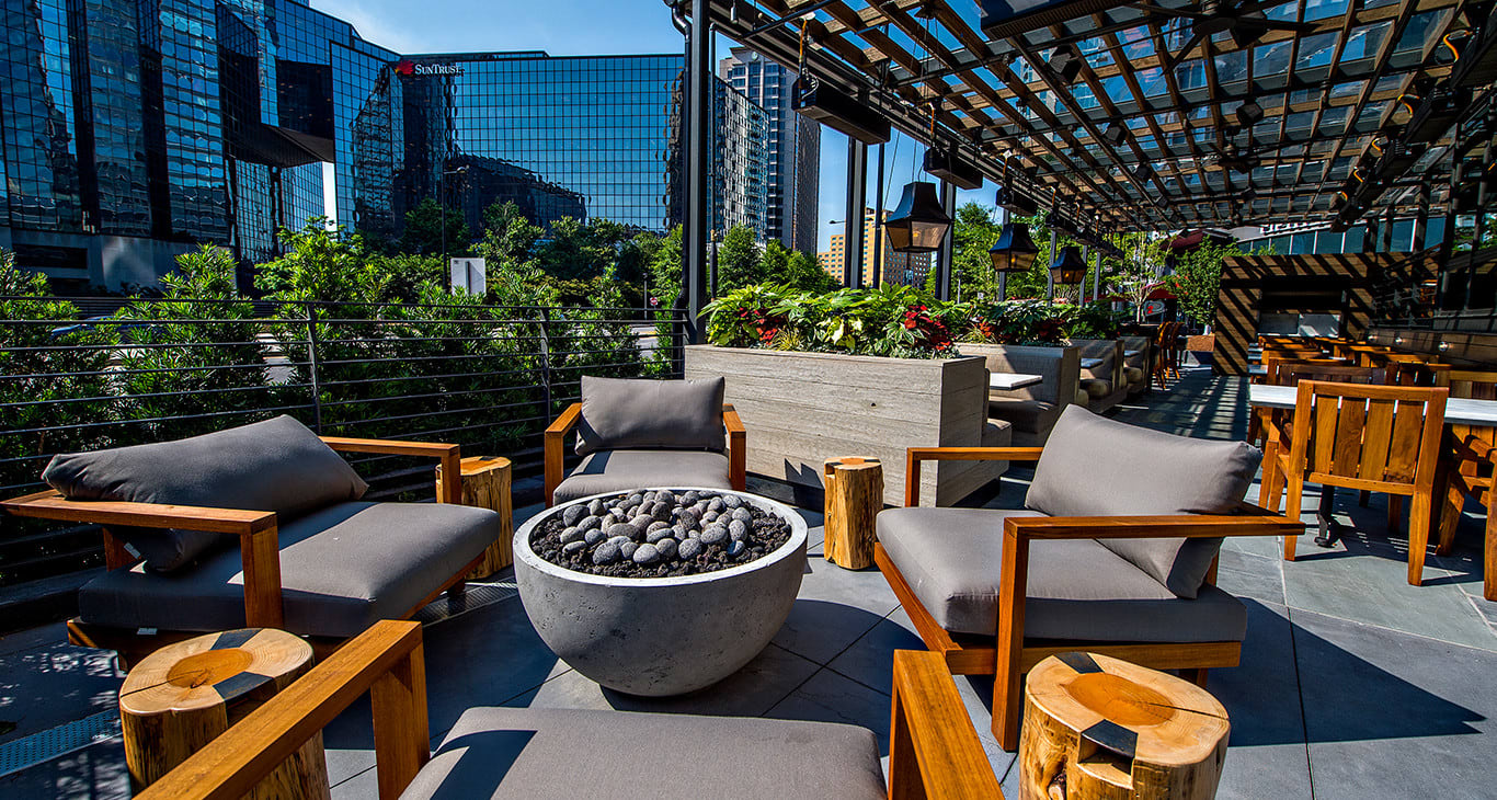 Modern rooftop patio with wooden furniture, fire pit, and city skyline view in Atlanta, Georgia.