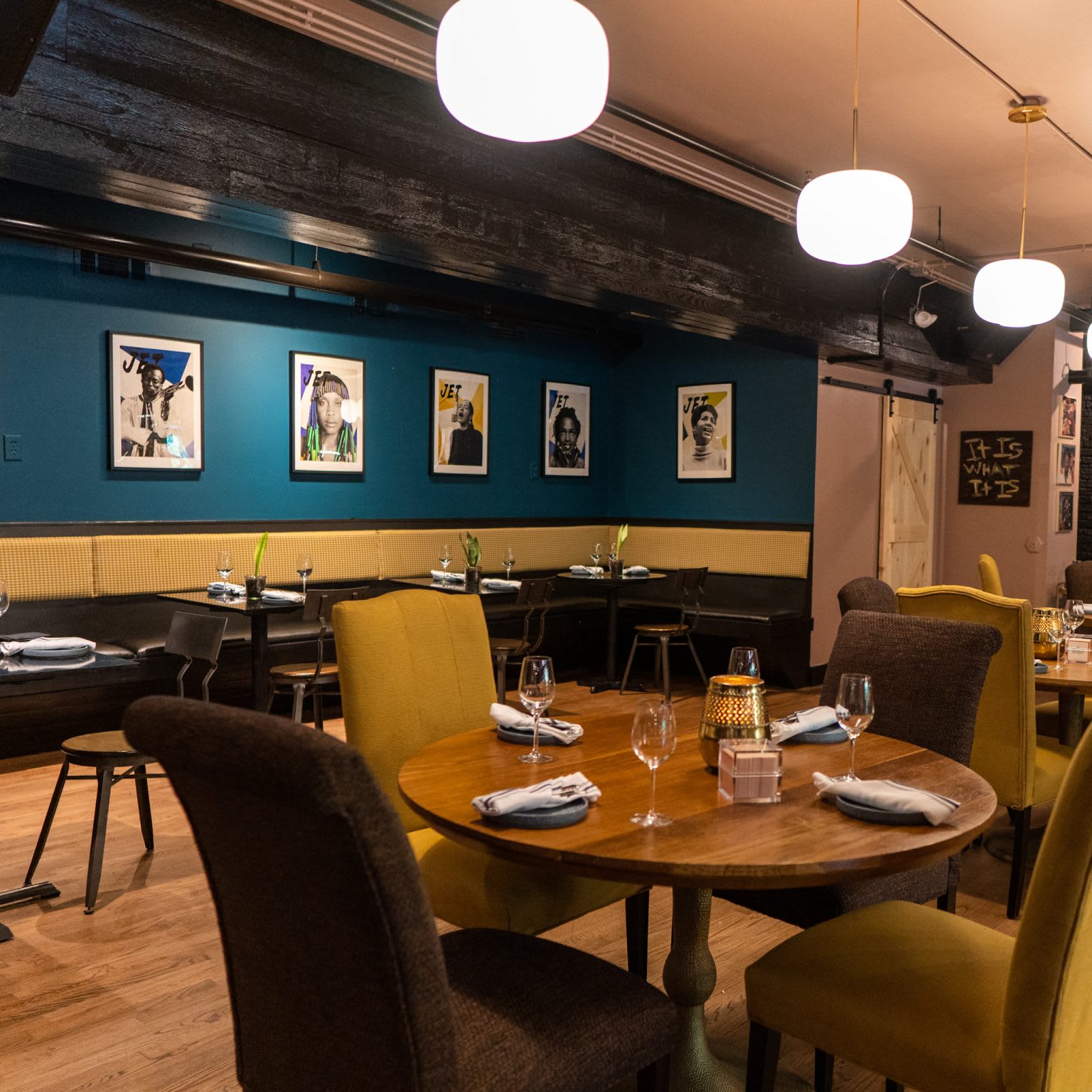 A cozy restaurant interior with round wooden tables, yellow chairs, and blue walls featuring framed portraits in Atlanta, Georgia.