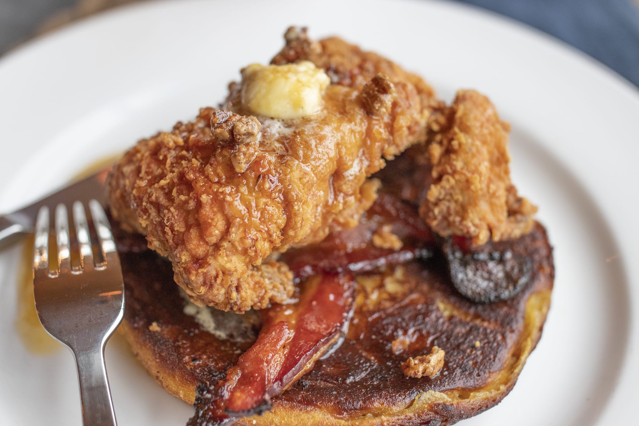 Crispy fried chicken with bacon and syrup on a pancake, served with a fork in Atlanta, Georgia.
