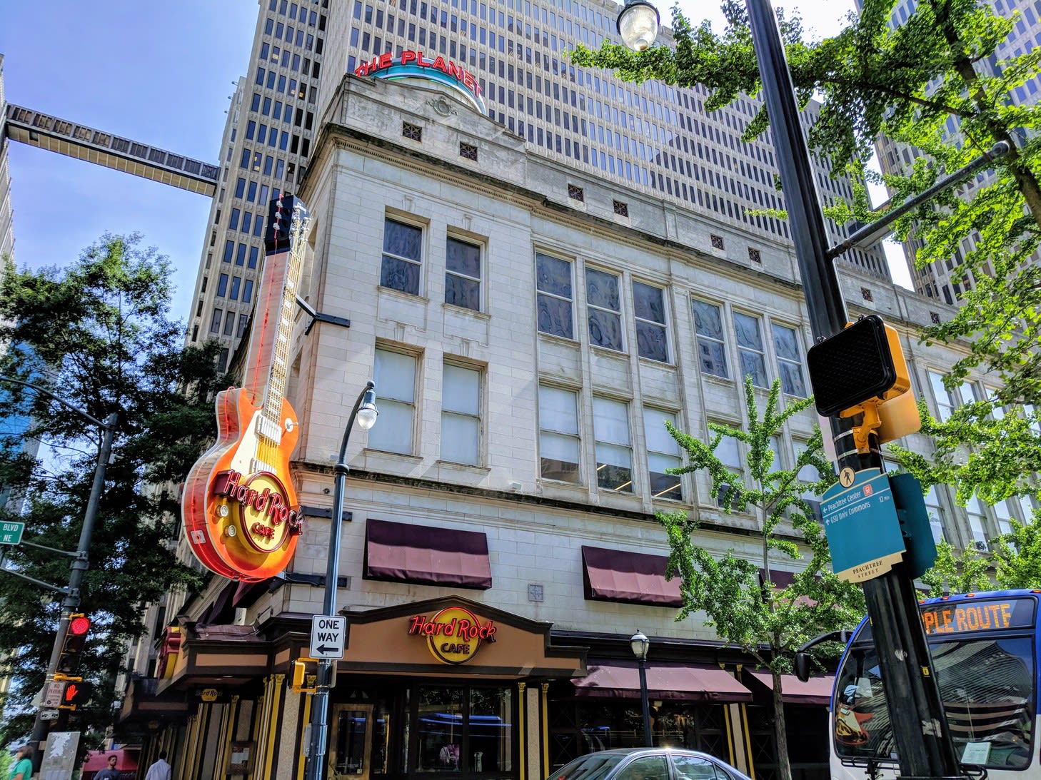 A city street scene featuring a Hard Rock Cafe with a large guitar sign and a tall building with a planet-themed sign in Atlanta, Georgia.