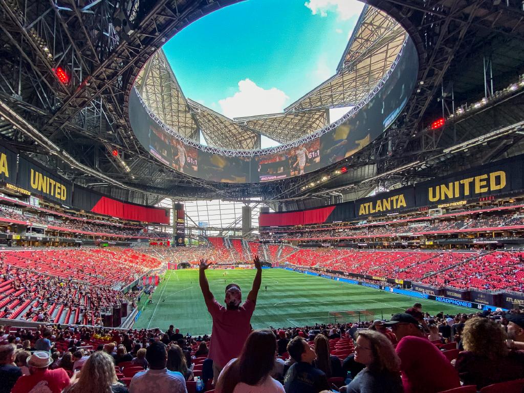 A packed stadium with a unique roof design and a fan celebrating on the field in Atlanta, Georgia.
