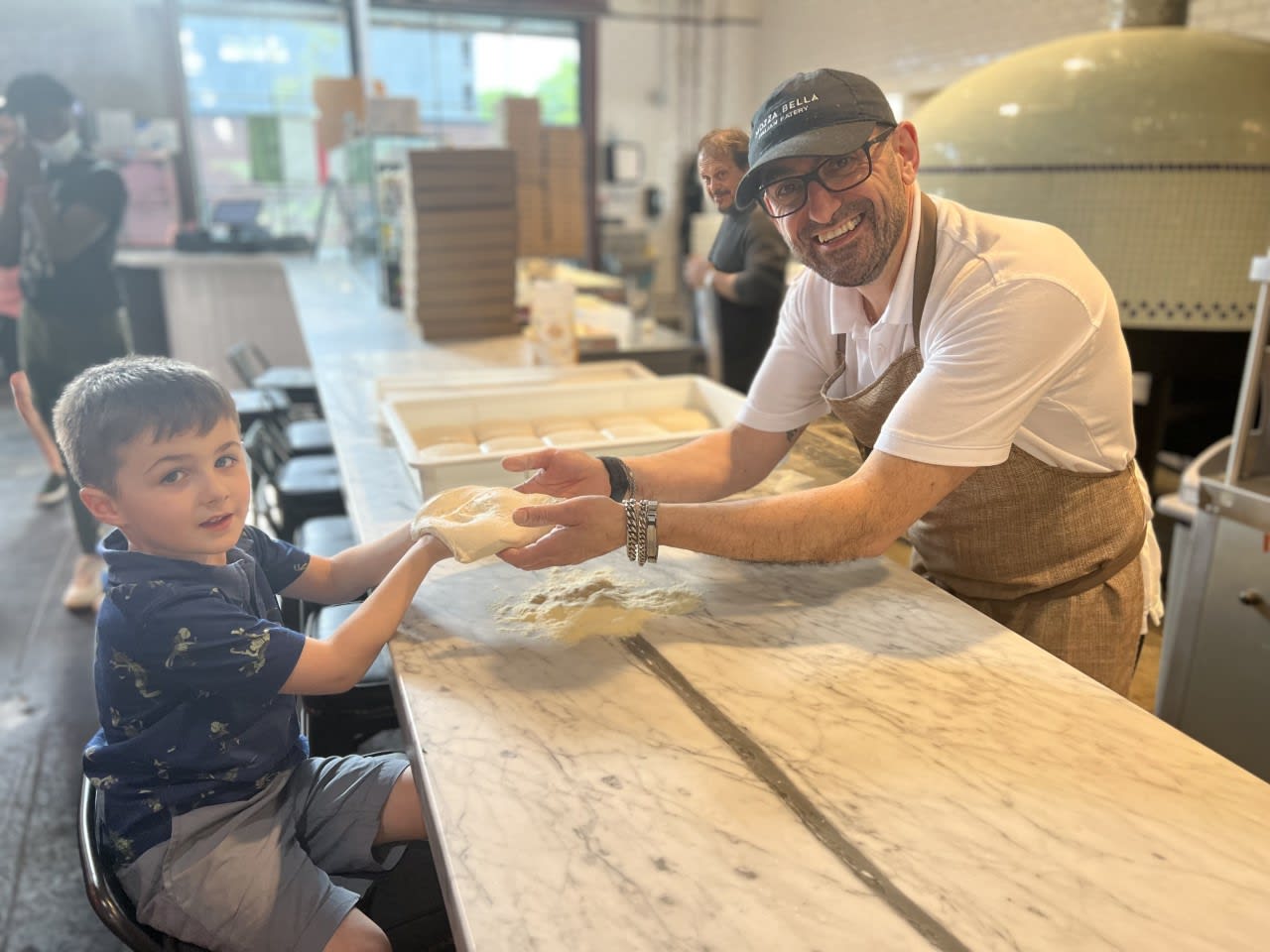 A young boy and a man in an apron knead dough on a marble counter in a bakery in Atlanta, Georgia.