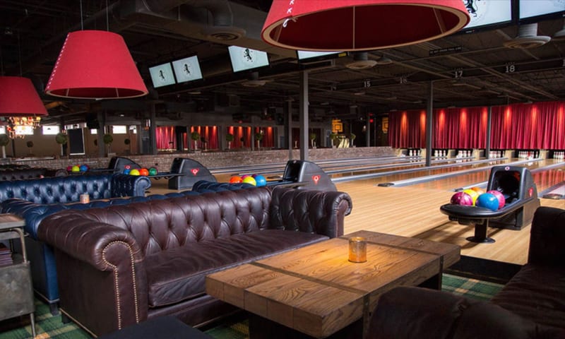 A modern bowling alley with leather sofas, wooden tables, and colorful bowling balls in Atlanta, Georgia.