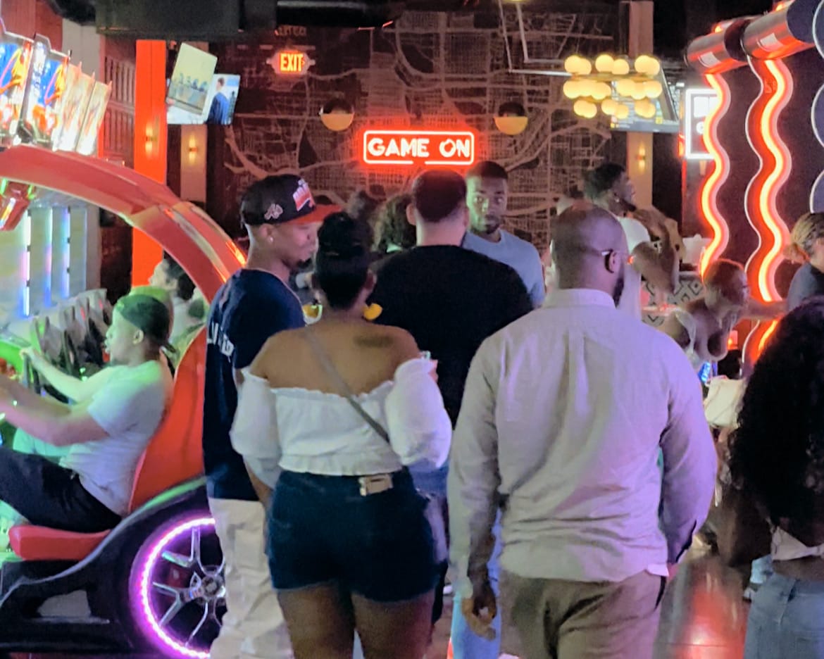 Crowded arcade with neon lights, video games, and people playing and socializing in Atlanta, Georgia.