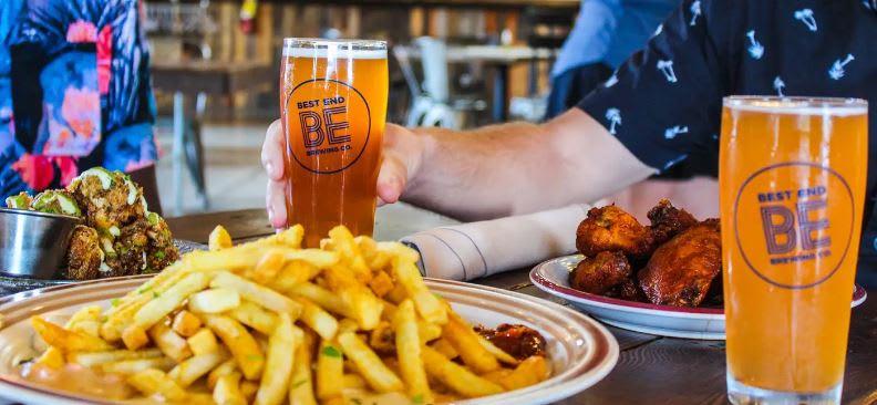 A person holds a glass of beer next to plates of fries and chicken wings in Atlanta, Georgia.