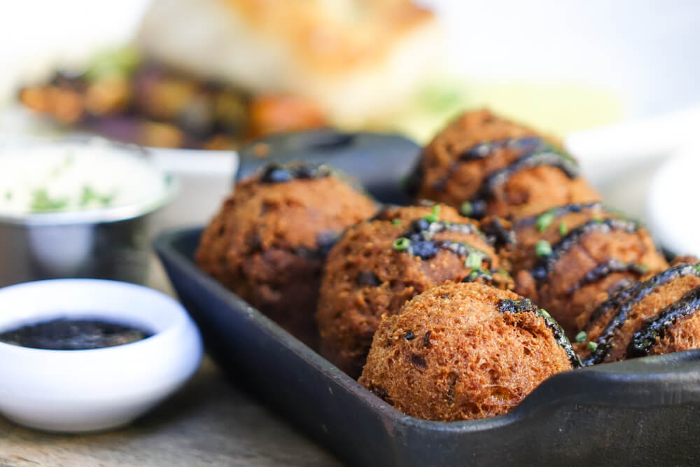 A cast iron skillet holds crispy fried balls garnished with herbs and a dark sauce in Atlanta, Georgia.