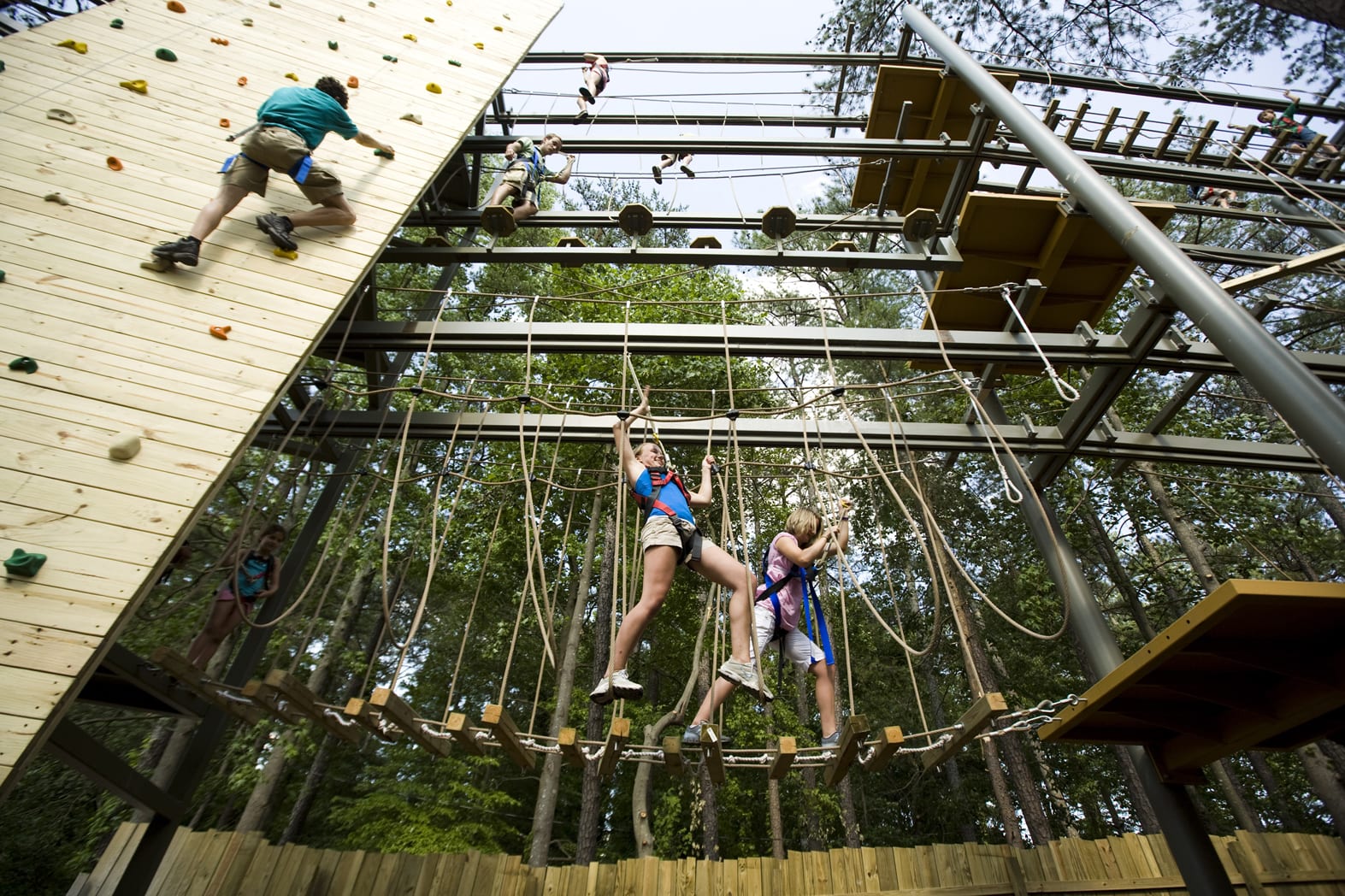 People are climbing a tall wooden structure with ropes and platforms in a forest in Atlanta, Georgia.