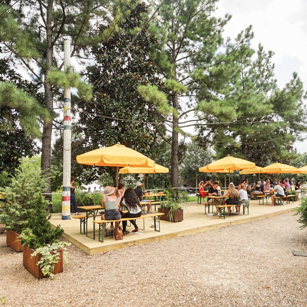 Outdoor patio with wooden benches, yellow umbrellas, and people dining under trees in Atlanta, Georgia.