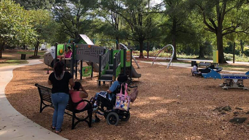 A family enjoys a sunny day at a playground with accessible equipment and a variety of colorful structures in Atlanta, Georgia.