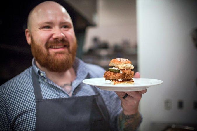 A smiling chef proudly presents a plate with a chicken sandwich in Atlanta, Georgia.