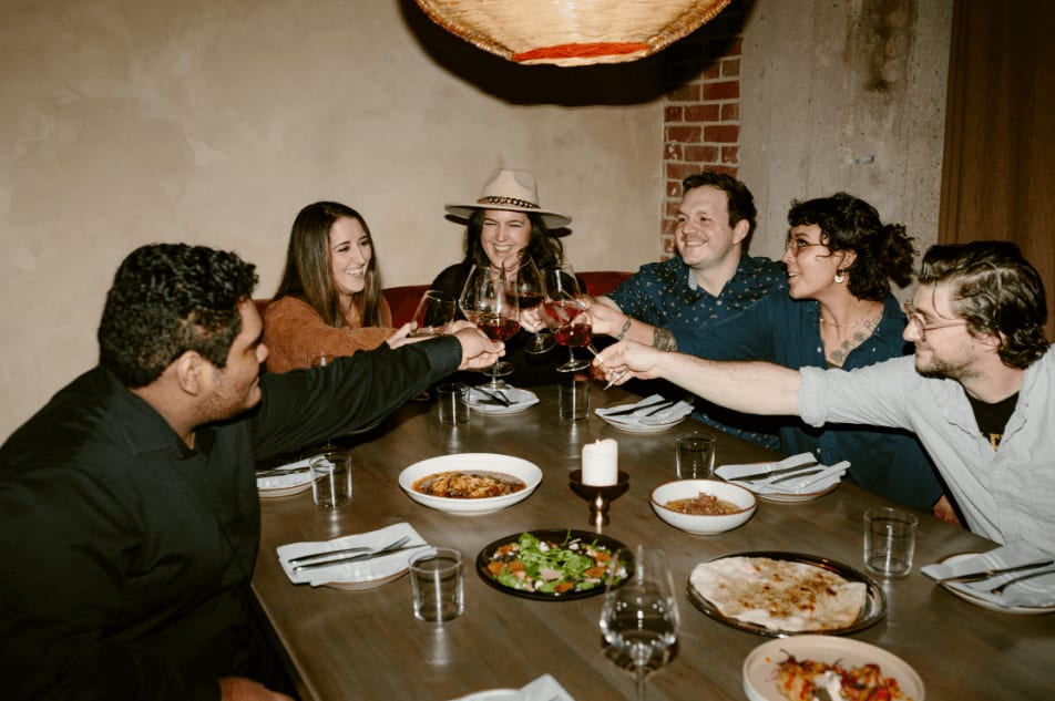 A group of six friends enjoys a meal together, raising their glasses in a toast in Atlanta, Georgia.