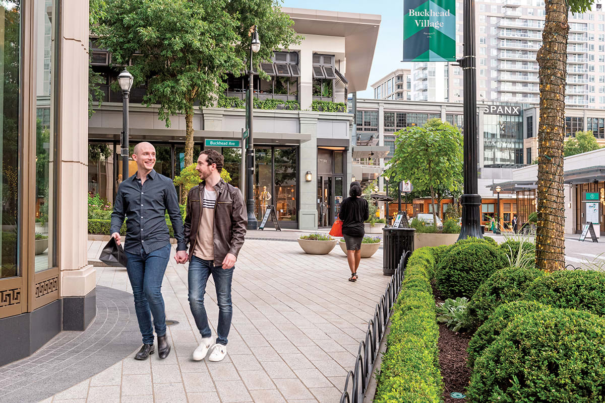 Two men holding hands walk down a tree-lined pedestrian street in an urban shopping area in Atlanta, Georgia.