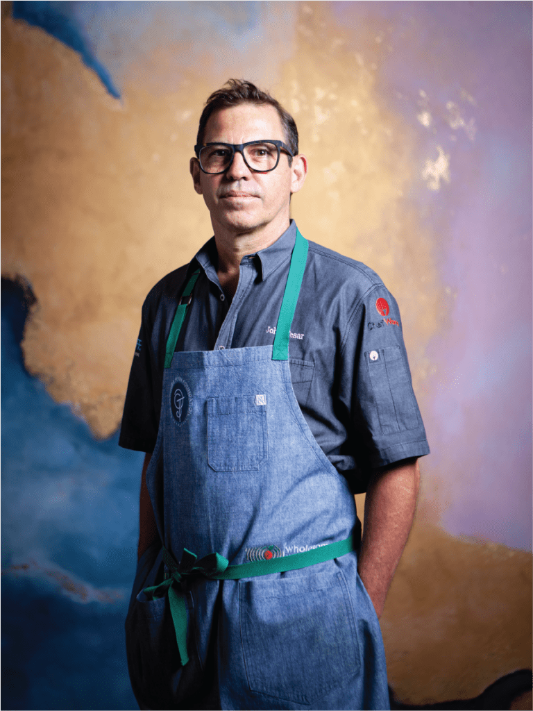 A man wearing a denim apron and glasses stands against a colorful abstract background in Atlanta, Georgia.